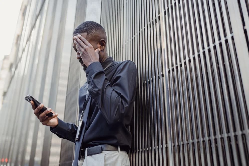 A worried man checking his phone with a hand on his forehead, illustrating a buyer waiting for a reply